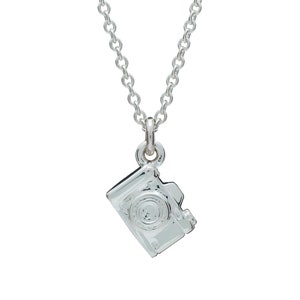 May include: A silver-colored necklace featuring a small camera pendant. The pendant is a detailed miniature replica of a camera, with visible lens and body details. The chain is a delicate, linked design.