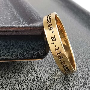 May include: A gold band ring with the inscription "24.4582 -118.05849 &deg; N".