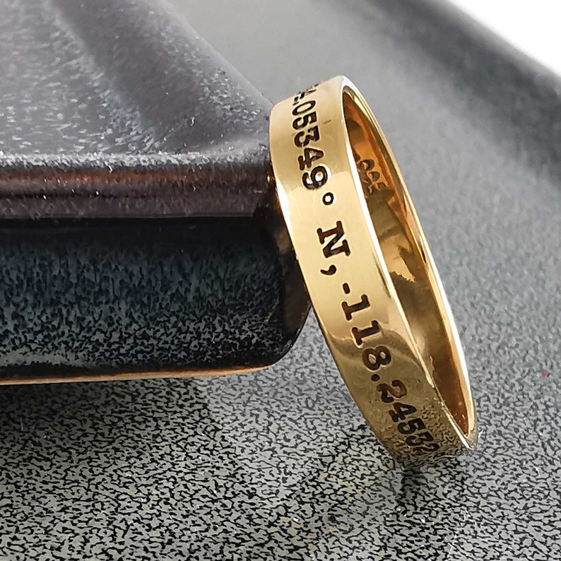 May include: A gold band ring with the inscription "24.4582 -118.05849 &deg; N".