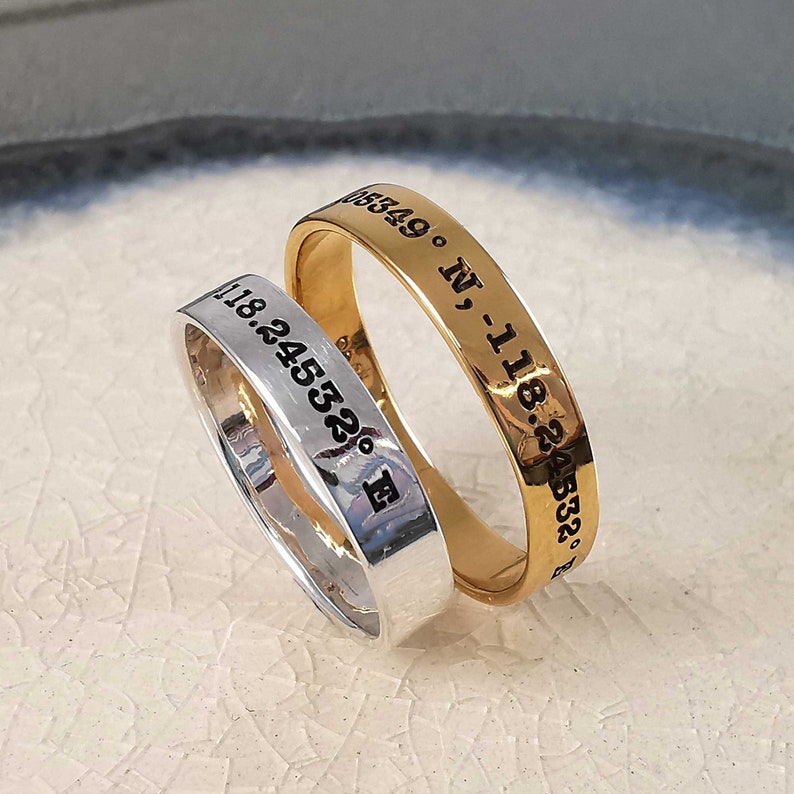 May include: Two rings with engraved coordinates. The top ring is gold and the bottom ring is silver.
