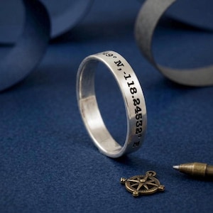 coordinates engraved silver ring band on blue background with compass and ribbon