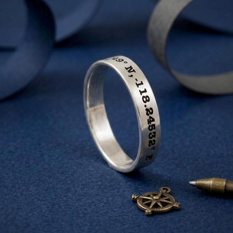 coordinates engraved silver ring band on blue background with compass and ribbon