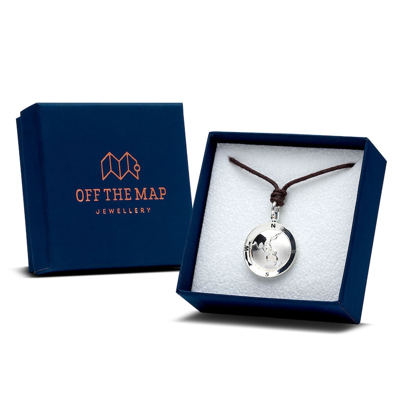 May include: A silver pendant necklace with a world map design, displayed in a navy blue gift box. The box has the text "OFF THE MAP JEWELLERY" printed on it. The necklace is on a brown cord.