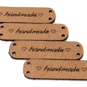 May include: Four brown leather labels with the word "handmade" and a heart symbol on each. The labels have two holes on each side for sewing.