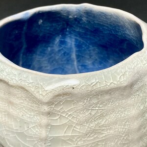 May include: A white ceramic bowl with a blue glaze inside. The bowl has a textured, crackled surface.