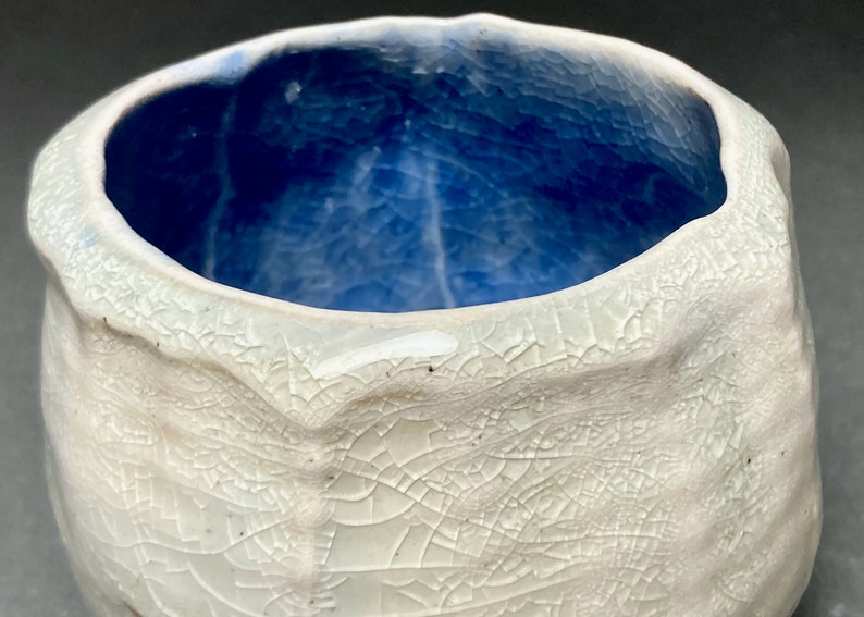 May include: A white ceramic bowl with a blue glaze inside. The bowl has a textured, crackled surface.