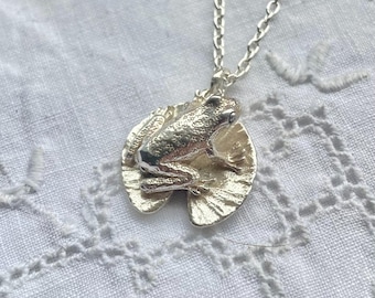 May include: A silver necklace with a frog sitting on a lily pad pendant.
