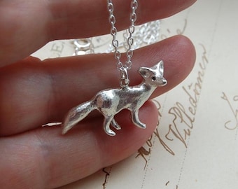 Op de afbeelding: Een zilverkleurige vos hanger ketting. De vos bedel is gedetailleerd en driedimensionaal, met zichtbare oren, poten en staart. De ketting is ook zilverkleurig en ziet er delicaat uit.
