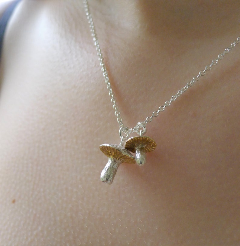 May include: A silver chain necklace with a gold and silver mushroom charm pendant.