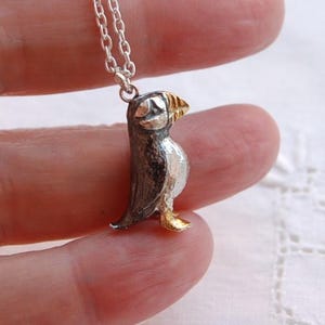 Op de afbeelding: Zilveren papegaaiduiker hanger met een goudkleurige snavel en poten, hangend aan een fijne zilveren ketting. Het lichaam van de vogel is gedetailleerd in zwart en zilver. Een charmant sieraad met vogelthema.