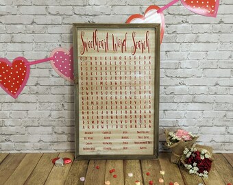 Puede incluir: Un letrero de madera con un crucigrama de búsqueda de palabras rojo y blanco titulado "Sweetheart Word Search". El rompecabezas presenta palabras relacionadas con el amor y el Día de San Valentín, como "love", "hearts", "kisses", "candy" y "flowers".