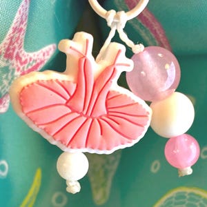 May include: A charm featuring a pink and white ballerina tutu design, accented with pink and white beads. The charm is attached to a white ring, perfect for a keychain or accessory.