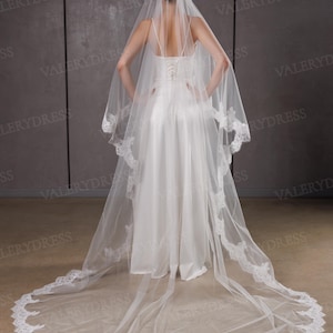 May include: A white wedding veil with a delicate lace trim, cascading down to the floor. The veil is paired with a white bridal gown. The text "VALERYDRESS" is visible in the background.