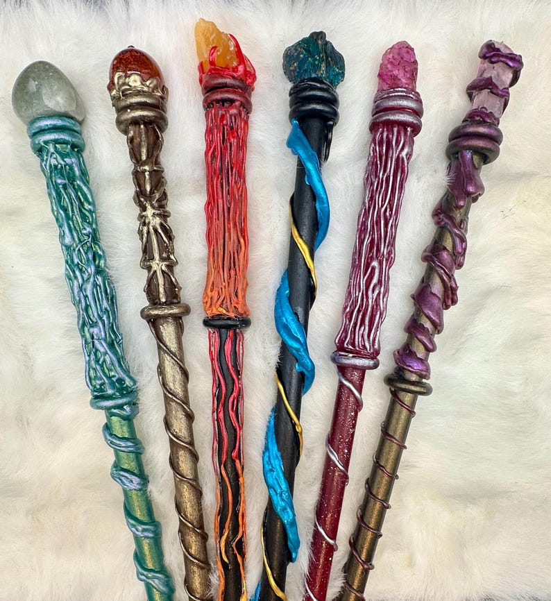 K&ouml;nnte beinhalten: Eine Sammlung von sieben handgefertigten Zauberst&auml;ben mit einzigartigen Designs. Jeder Zauberstab hat ein anderes Farbschema, darunter Gr&uuml;n, Braun, Rot, Schwarz und Lila, und ist mit einem Kristall oder Edelstein gekr&ouml;nt. Die Zauberst&auml;be weisen komplizierte Details und Spiralmuster auf.