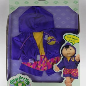Könnte beinhalten: Ein Cabbage Patch Kids Baby Playtime Fashion Set in einer Box. Das Set enthält eine lila Kapuzenjacke, ein gelbes Hemd und rosa Shorts mit Sternmustern. Auf der Box steht "For Babies Only!"