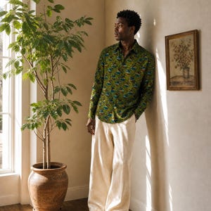 Peut inclure: Une chemise à manches longues boutonnée d'un vert vif avec un motif circulaire répétitif dans des tons de bleu, orange et marron, associée à un pantalon ample blanc cassé et des chaussures de ville en cuir noir.