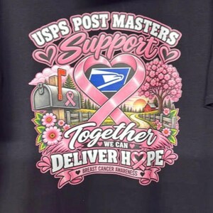 以下が含まれることがあります： USPS POST MASTERS SUPPORT TOGETHER WE CAN DELIVER HOPE BREAST CANCER AWARENESSという文字がプリントされた黒いTシャツ。デザインには、ピンクのリボン、郵便受け、ピンクの花が咲く木、USPSのイーグルロゴが含まれています。