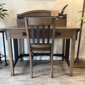 May include: A wooden desk with a black metal frame and a matching wooden chair. The desk has a drawer and a shelf above the drawer. The chair has a slatted back and a solid seat.