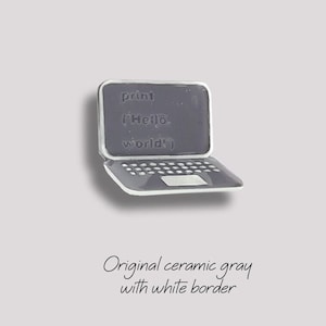 May include: A ceramic laptop charm in grey with a white border. The screen displays the code "print('Hello, world')".