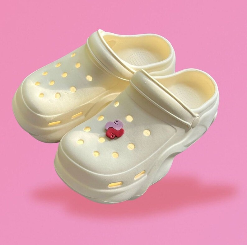 Puede incluir: Dos pares de zuecos blancos de plataforma con un dije de coraz&oacute;n rosa y rojo en uno de los zuecos.