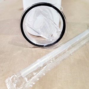 May include: A clear plastic lid with a black rim and a clear plastic straw in a plastic wrapper. The lid has a small, clear plastic tab on the side.