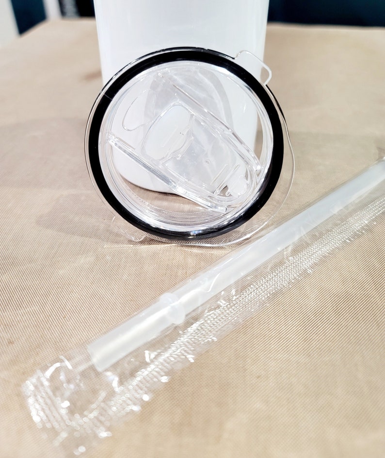 May include: A clear plastic lid with a black rim and a clear plastic straw in a plastic wrapper. The lid has a small, clear plastic tab on the side.