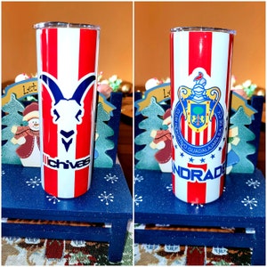 May include: Two stainless steel tumblers with a red, white, and blue striped design. One tumbler features a goat head logo with the word "Chivas" below it. The other tumbler features a crest with the text "Club Deportivo Guadalajara SA de CV" and the word "Norad" below it.