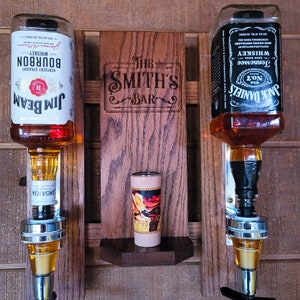 Puede incluir: Un expositor de bar de madera con dos dispensadores de botellas de licor, uno para Jim Beam Bourbon y otro para Jack Daniel's Tennessee Whiskey. Una peque&ntilde;a repisa contiene un objeto decorativo, y el letrero de madera dice "The Smith's Bar."
