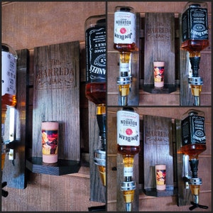Puede incluir: Un expositor de bar de madera con m&uacute;ltiples dispensadores de botellas de licor. El expositor presenta botellas de Jack Daniel's y bourbon Jim Beam. El fondo de madera est&aacute; grabado con "The Barreda Bar". Tambi&eacute;n hay una peque&ntilde;a taza decorativa.