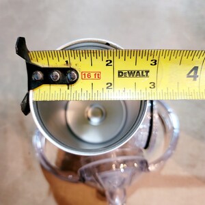 May include: A yellow tape measure with black markings and the text "DEWALT" and "16 ft" is used to measure the diameter of a silver metal cup with a clear plastic lid.