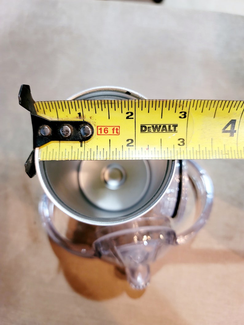 May include: A yellow tape measure with black markings and the text "DEWALT" and "16 ft" is used to measure the diameter of a silver metal cup with a clear plastic lid.