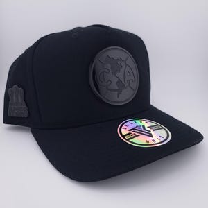 May include: Black baseball cap with a round emblem featuring a map and the letters "CA". The cap has a flat brim and a small emblem on the side. A holographic sticker is on the brim.