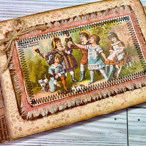 Pu&ograve; includere: Un diario in stile vintage con una copertina in pelle marrone e una patta in tessuto decorativa. La patta presenta un bordo cucito e un bordo sfrangiato. Il diario ha un titolo sulla copertina che recita "The Shoe Co.". La patta presenta un'illustrazione vintage di bambini che giocano con i campanelli. L'illustrazione &egrave; della "Union Pacific Tea Company".