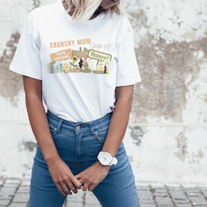 以下が含まれることがあります： 農場のシーンと「Crunchy Mom Starter Kit 100% Organic Farm Natural!」というテキストが描かれた白いTシャツ