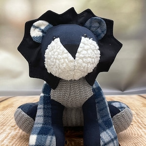 May include: A plush blue and grey lion toy with a white face and black eyes. The lion is sitting with its legs crossed and has a blue and white plaid pattern on its body.