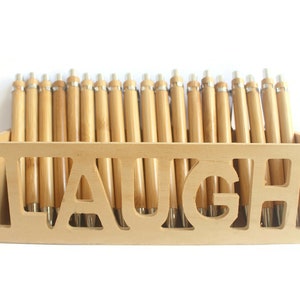 Op de afbeelding: Een houten doos met het woord "LAUGH" uitgesneden aan de voorkant. De doos is gevuld met bamboe pennen.