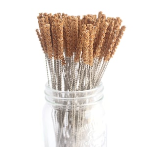May include: A glass jar filled with a bunch of brown and silver cleaning brushes. The brushes are made of natural materials and are designed for cleaning narrow spaces.