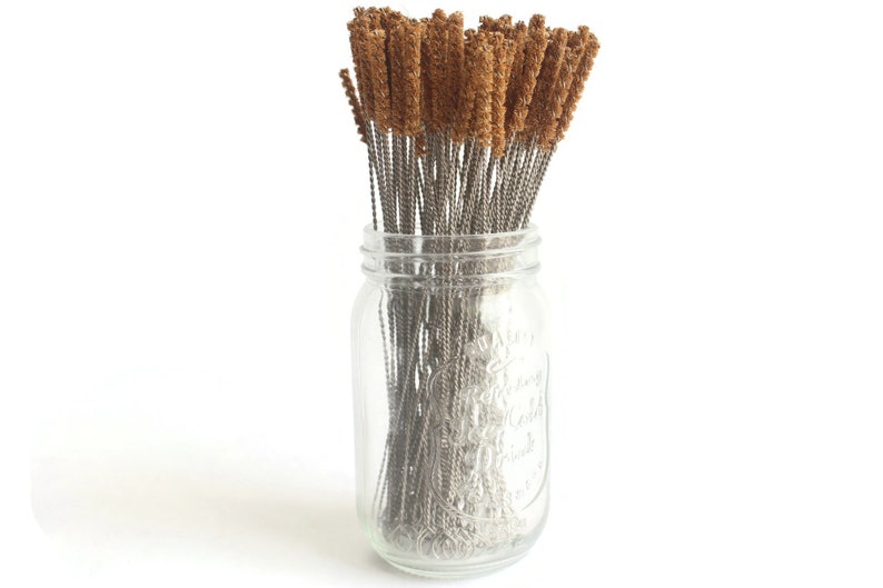 May include: A glass jar filled with a bundle of brown and silver cleaning brushes. The brushes are made of a soft, bristled material and are designed for cleaning narrow spaces.