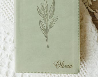 May include: A sage green notebook with a smooth, matte finish featuring a centered, dark green line-art illustration of a leafy plant. The name Olivia is engraved in a cursive script font in the bottom right corner of the front cover.
