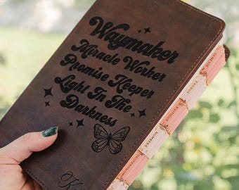 May include: A dark brown leather-bound book featuring the engraved text Waymaker Miracle Worker Promise Keeper Light In The Darkness, a butterfly illustration, and the name Katie. The book includes light pink tabbed page dividers.