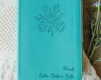 May include: A teal-colored journal with a smooth, leather-like cover featuring an embossed floral design in the center. The bottom right corner is personalized with the name Brenda and the names Colton, Caden & Collin in a cursive script font.