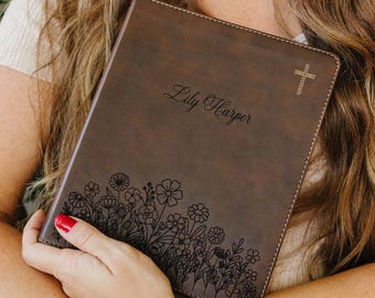 May include: A dark brown leather-like book cover featuring a laser-engraved floral pattern along the bottom edge, the name Lily Harper in script font in the center, and a small cross symbol in the top right corner with visible stitching.
