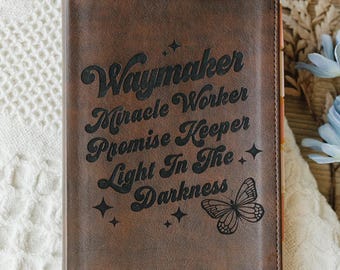 May include: A brown rectangular journal cover featuring the engraved text Waymaker Miracle Worker Promise Keeper Light In The Darkness, accompanied by a butterfly illustration and small star icons, with the name Katie engraved in the bottom corner.