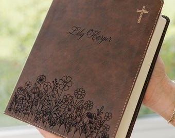 May include: A brown leather-like book cover featuring a laser-engraved floral pattern along the bottom edge, the name Lily Harper in script font in the center, and a small cross symbol in the top right corner with visible stitching along the edges.