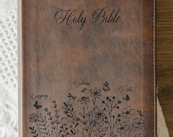 May include: A brown leather-look Bible featuring the text Holy Bible at the top, a black line-art illustration of wildflowers and butterflies with the names Dempsey, Callum, and Miller, and the text With God all things are possible Matthew 19:26.