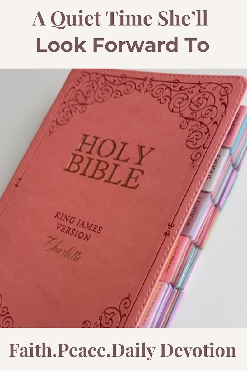 May include: A coral-colored Holy Bible, King James Version, with the name Charlotte embossed on the cover. The book features decorative scrollwork at the top and bottom, and includes multi-colored index tabs along the side for navigation.