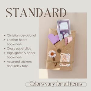 May include: A brown paper-wrapped package containing a Christian devotional, a purple leather heart bookmark, gold cross paperclips, a highlighter, a paper bookmark, assorted stickers, and index tabs, tied with twine and decorated with a daisy sticker.