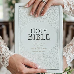 May include: A white Holy Bible with an embossed vine pattern on the cover. The text reads Holy Bible, King James Version, Mr. & Mrs. Williams, and September 26th, 2026. The cover features a decorative border and a central area for the text.