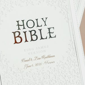 May include: A white Holy Bible with a textured vine pattern embossed on the cover. The text reads HOLY BIBLE, KING JAMES VERSION, Daniel & Lisa Rieathbaum, and June 6, 2026 - Forever in dark lettering centered on the front cover.