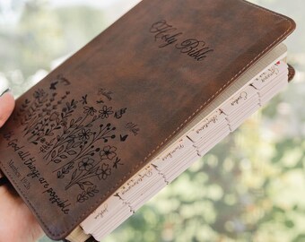 May include: A brown leather-like Bible with a dark brown floral engraving and the text "Holy Bible" and "With God all things are possible Matthew 19:26" on the front cover. The book features light-colored index tabs along the side edge.